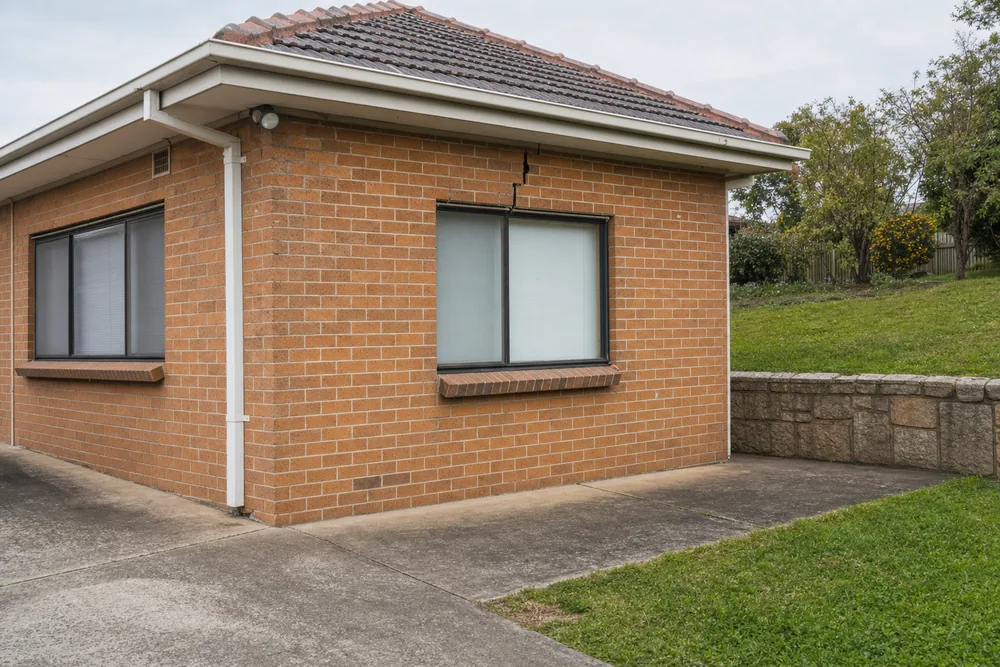 A brick house beside a driveway and a grassed bank with a stone-look retaining wall, with a thin crack above a window — underpinning, Wollongong. Illustrative example.